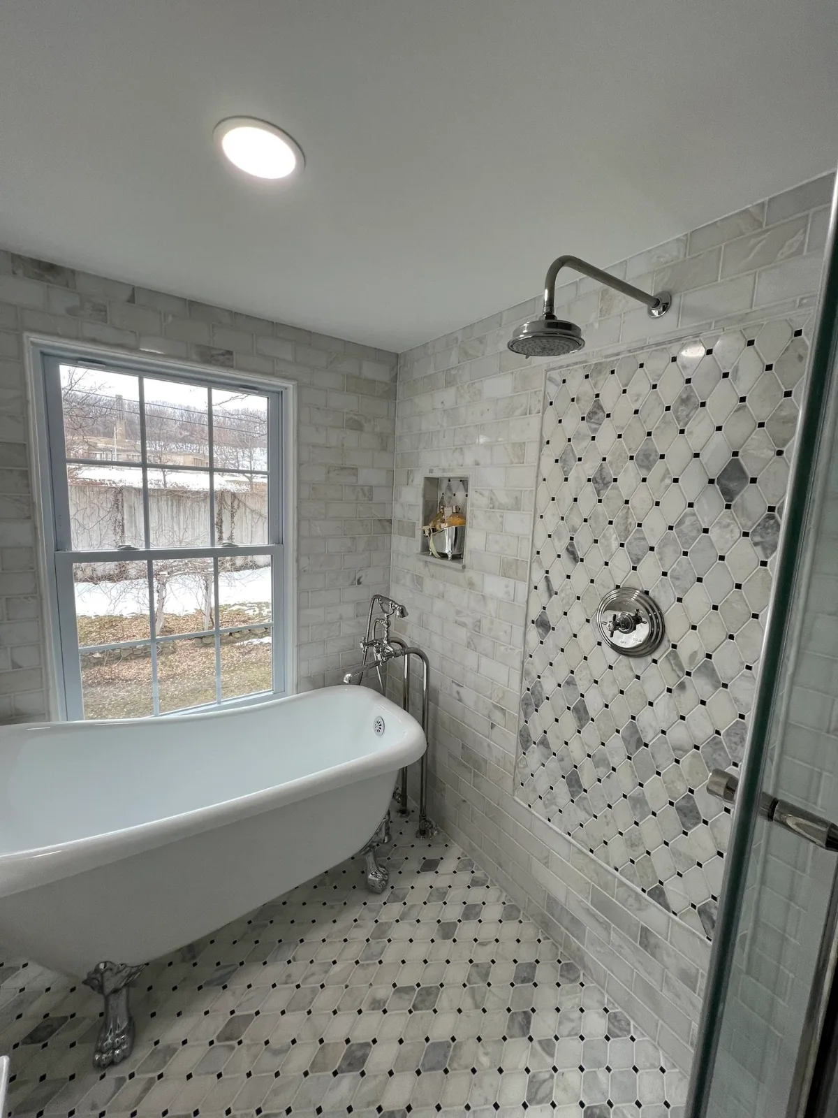 A bathroom with a clawfoot tub under a window and a diamond-pattern tile wall