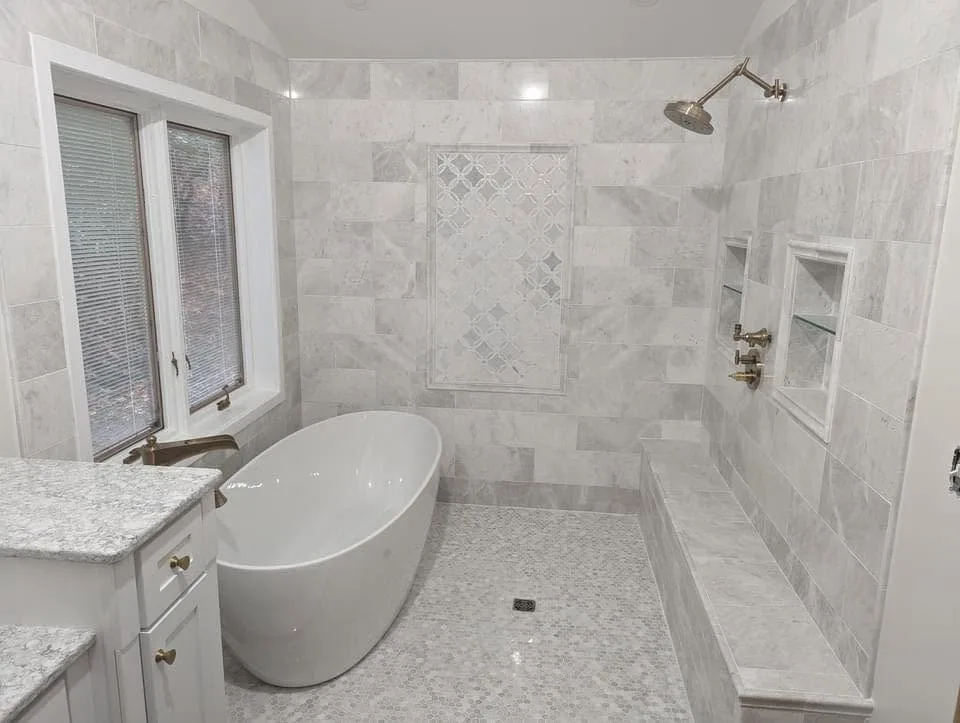 A bathroom with a freestanding tub, marble tile walls and a walk-in shower with a tiled bench