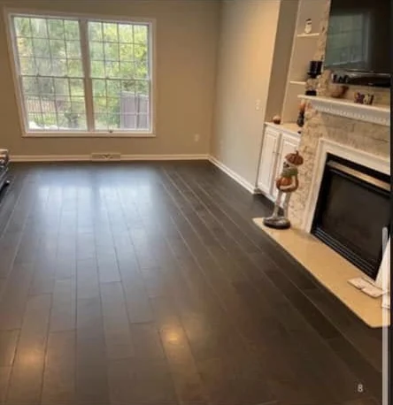 A living room with its new dark hardwood floor finished, beside a stone fireplace
