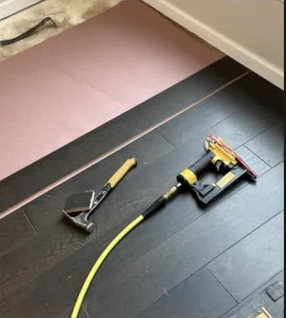 A flooring nailer and a mallet on new dark hardwood, beside pink underlay