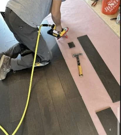 An installer nailing down dark hardwood boards over pink underlay