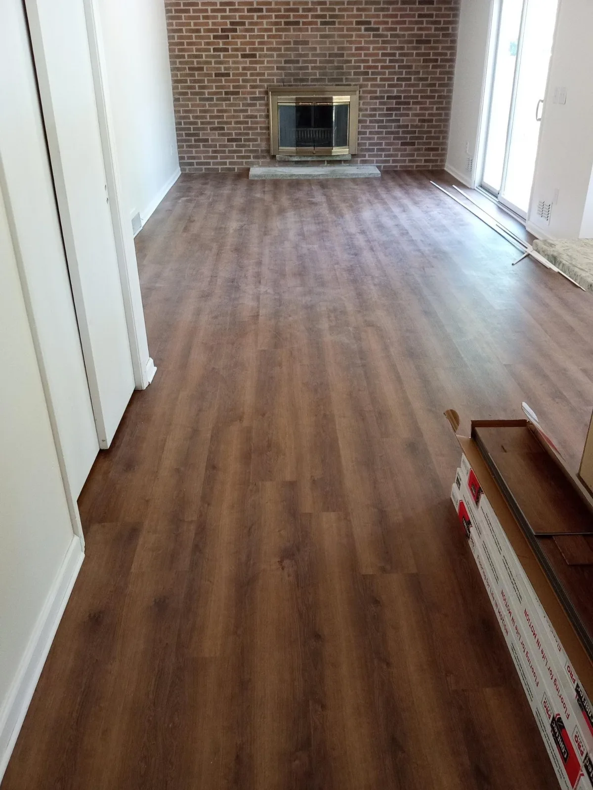 A living room with new wood plank flooring in front of a brick fireplace