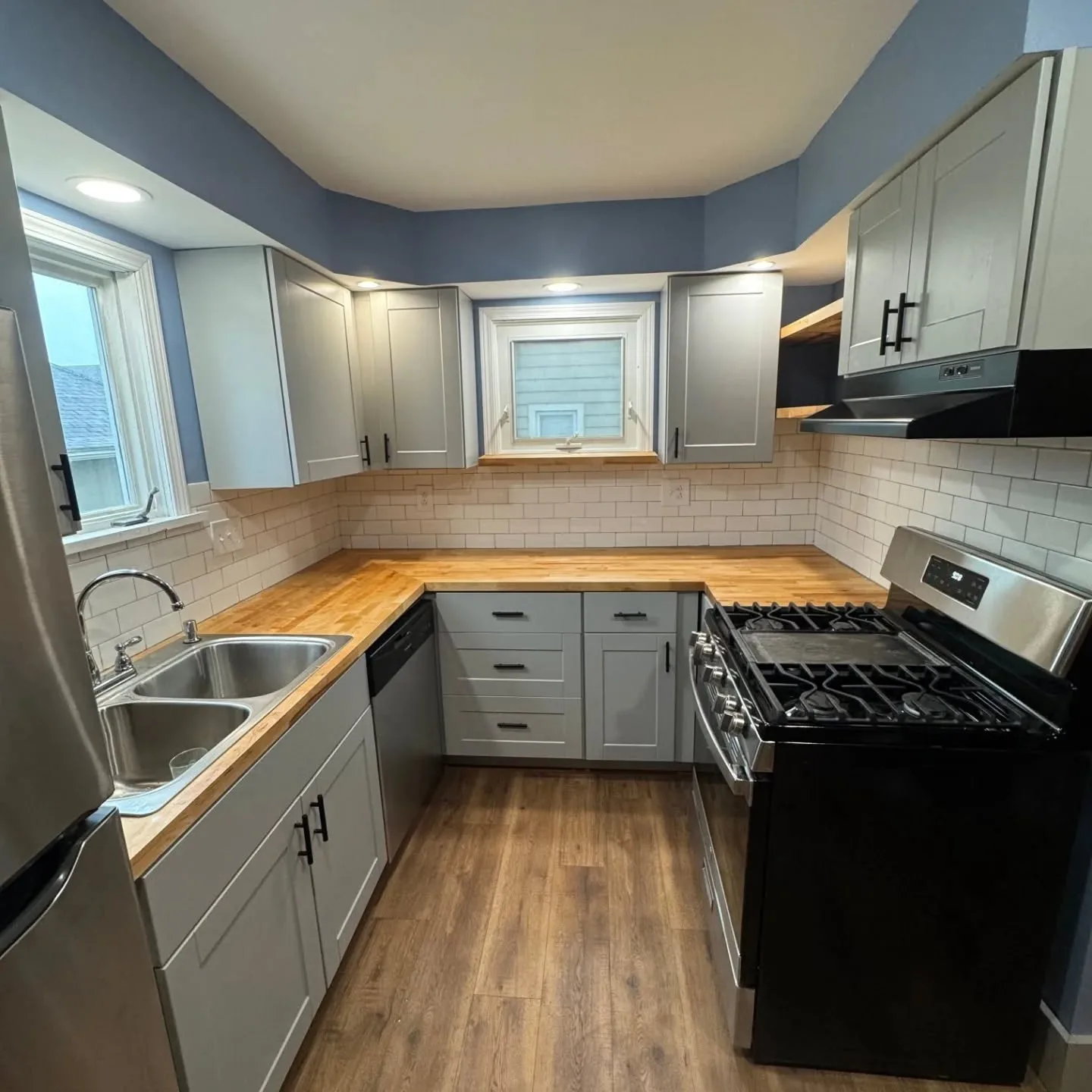 A kitchen with light gray shaker cabinets, butcher-block counters and a white subway tile backsplash