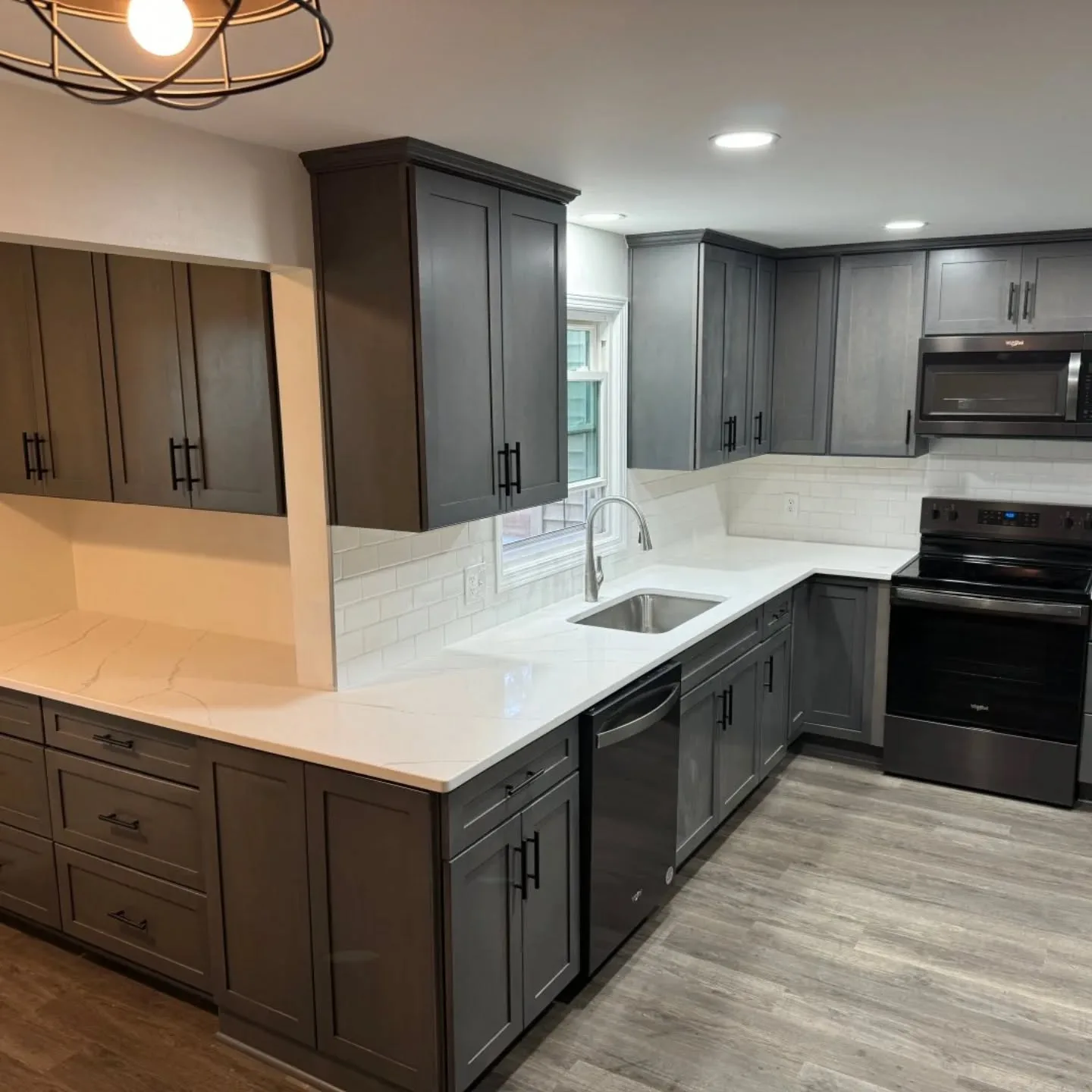 A kitchen with dark gray shaker cabinets, white quartz counters and a subway tile backsplash