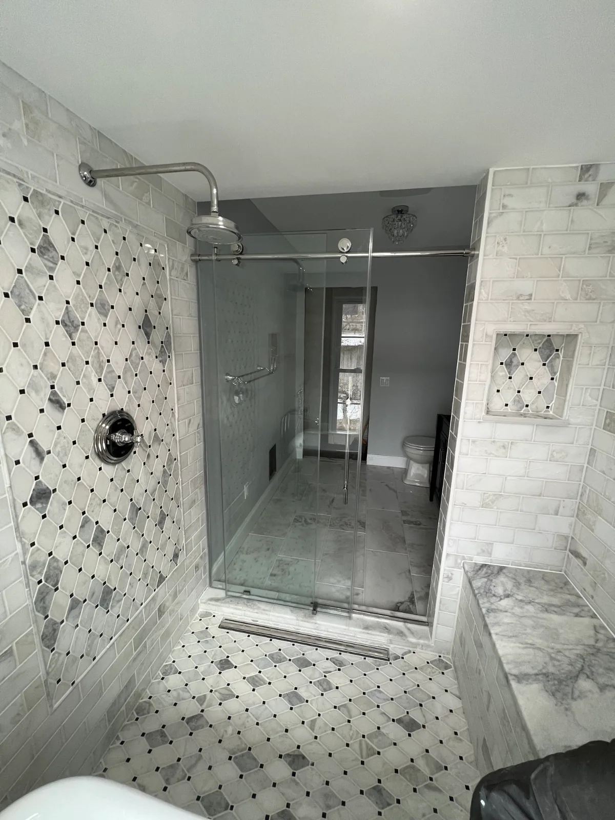 A glass walk-in shower with a diamond-pattern tile wall, a niche and a tiled bench