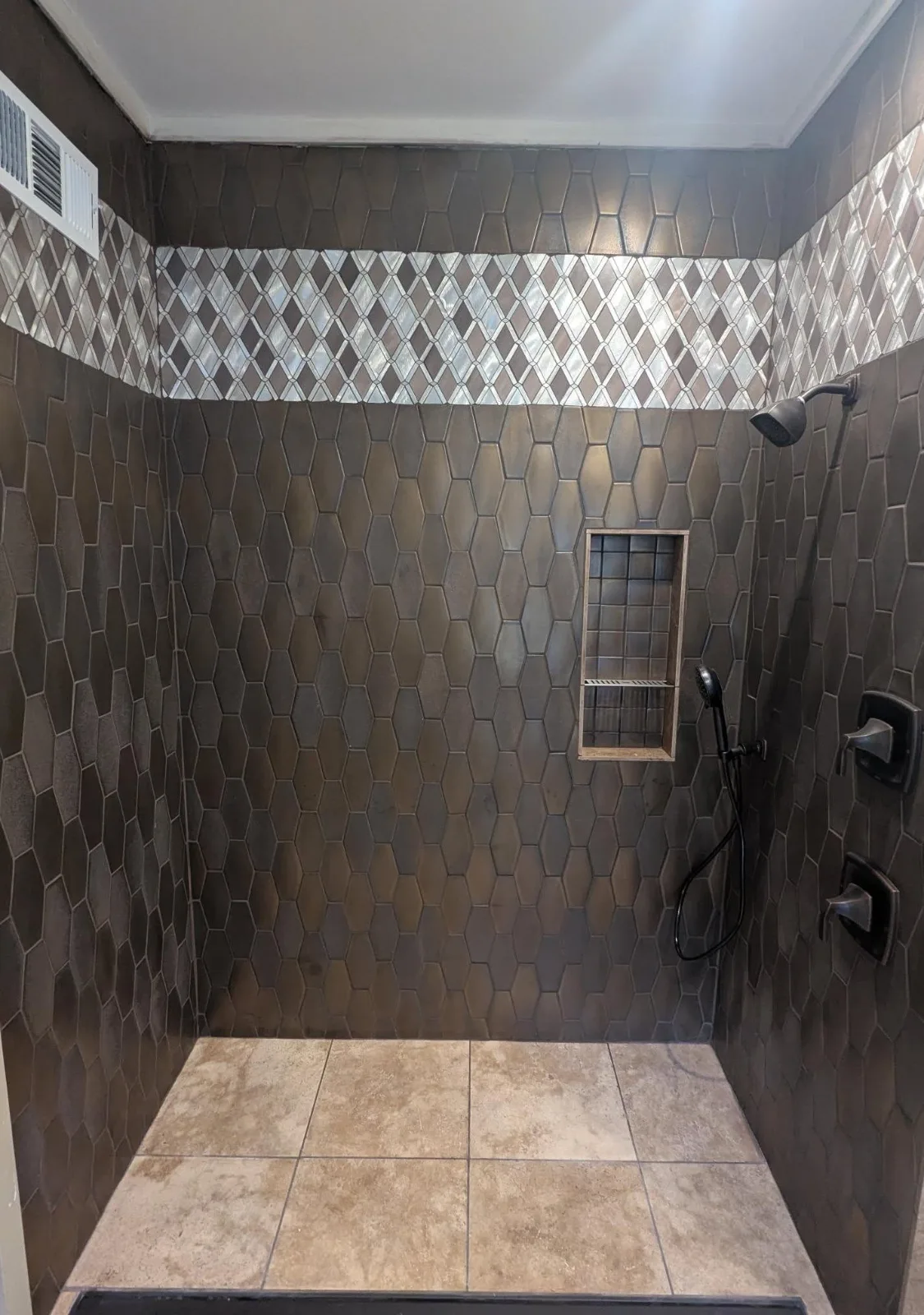 A walk-in shower in dark elongated hexagon tile, with a mosaic band and a tiled niche