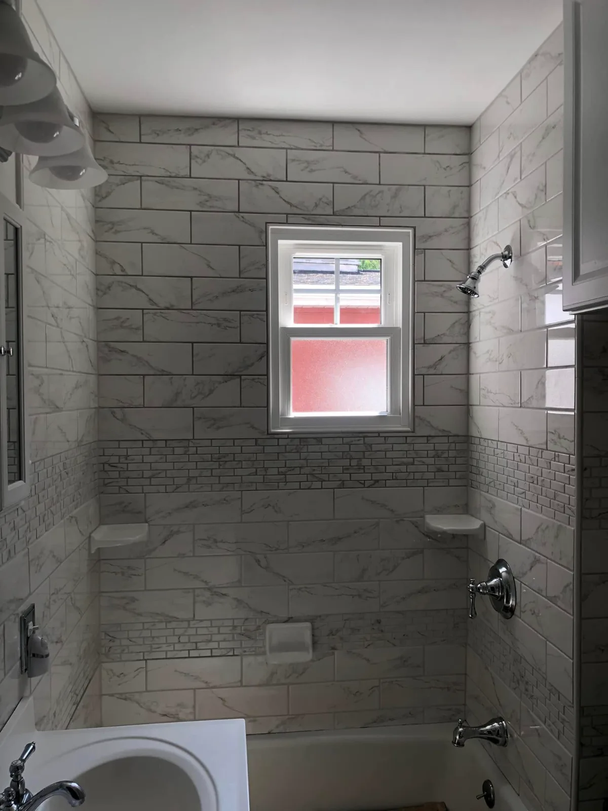 A tub and shower surround in white marble-look tile with a mosaic band, around a window